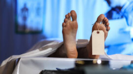 Medical examiner or forensic scientist with dead man's corpse in morgue.  He takes notes on medical chart after autopsy.